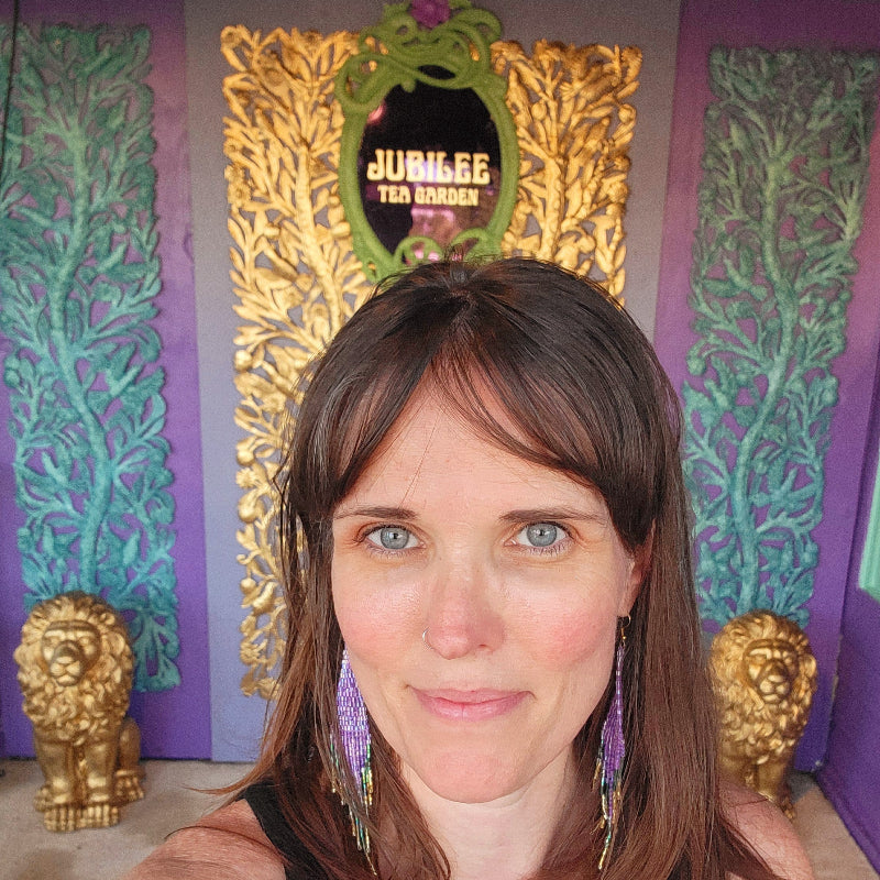 Woman with long brown hair in front of a decorative wall with gold and purple elements.