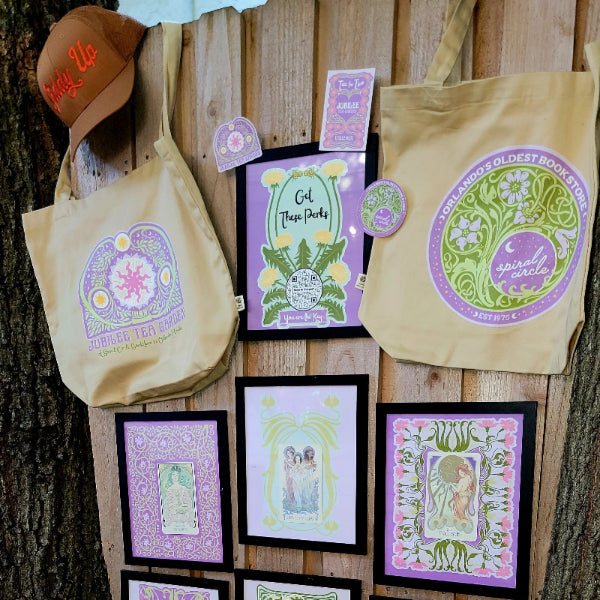 Framed artworks and tote bags with nature-themed designs on a wooden wall.